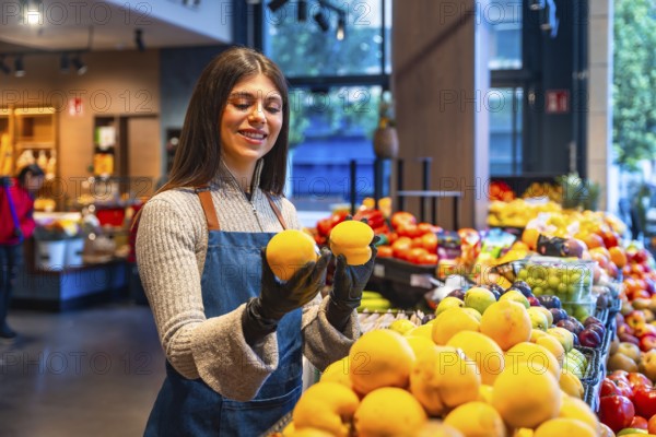 Produce worker wearing an apron and gloves arranging fresh oranges on a display, focusing on quality and presentation in a busy grocery store environment