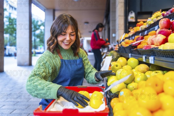 Smiling market worker in apron and gloves arranging fresh apples on a colorful outdoor fruit stall at a small local grocery, showcasing produce and friendly service