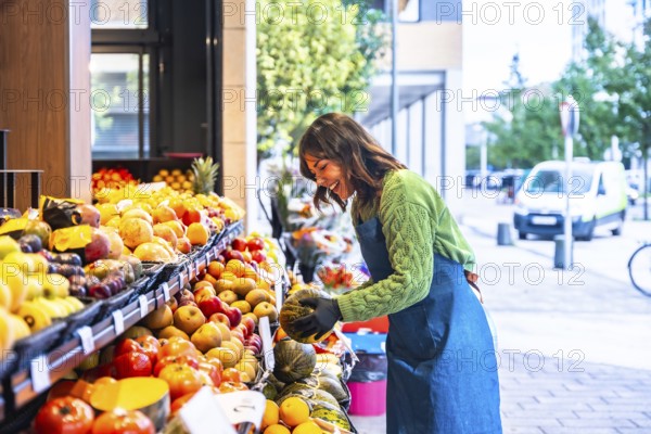 Woman smiling as she arranges colorful fresh fruits and vegetables on an outdoor market stand, showcasing healthy eating, local produce, and small business entrepreneurship
