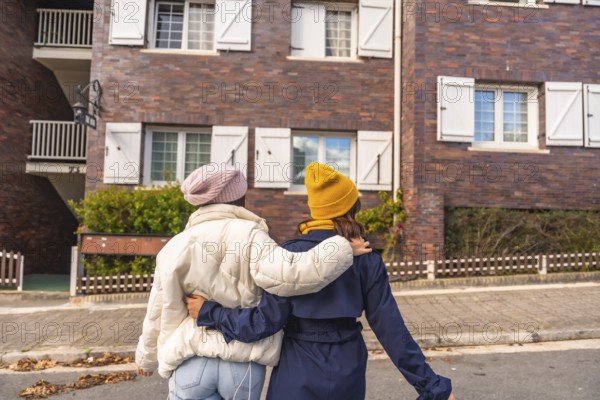 Two friends walking arm in arm down a european city street, enjoying an autumn day together in warm coats and beanies, sharing laughter and companionship