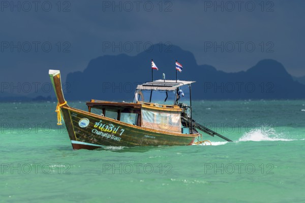Longtail boat in fast drive to the beach, behind it an approaching thunderstorm, Koh Ngai island, Andaman Sea, Satun province, southern Thailand, Thailand