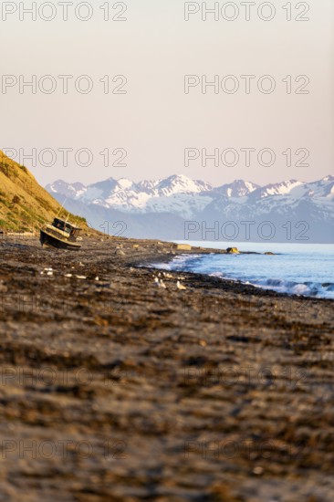 Boat on Anchor Point beach on Cook Inlet in the evening light, snowy mountain peaks, Anchor River State Recreation Area, Alaska, USA