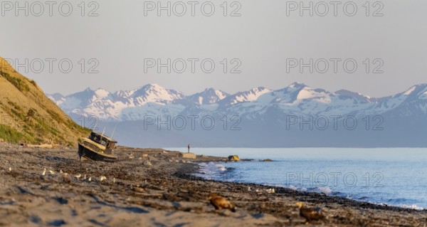 Boat on Anchor Point beach on Cook Inlet in the evening light, snowy mountain peaks, Anchor River State Recreation Area, Alaska, USA