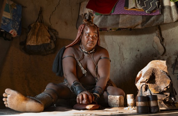Elderly Himba woman making red paste for skin care, in a hut, traditional Himba village, Kaokoveld, Kunene, Namibia