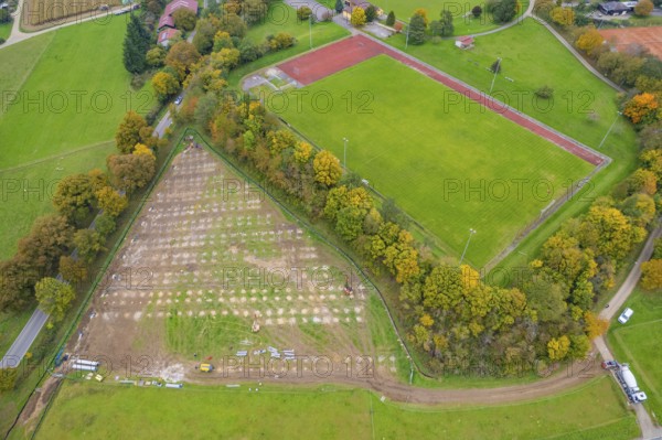 Aerial view of a sports field next to a large field and surrounded by autumn trees, PV Freifaechenanlage building, Weil der Stadt, Germany