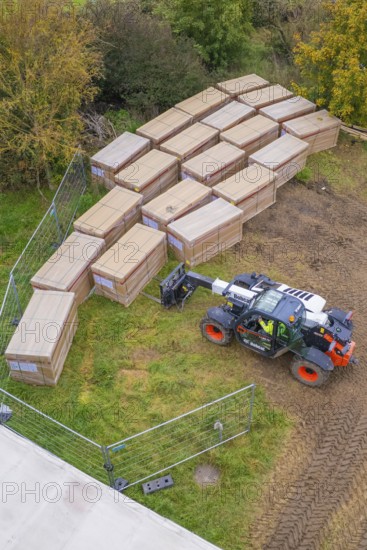 A forklift truck arranges stacked boxes on a fenced meadow in autumn, Bau PV Freifaechenanlage, Weil der Stadt, Germany