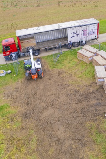 A forklift unloads boxes from a truck in a field next to a road, Bau PV Freifaechenanlage, Weil der Stadt, Germany