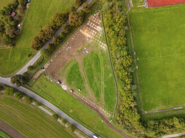 Aerial view of a field with construction next to a sports field, surrounded by trees, construction PV Freifaechenanlage, Weil der Stadt, Germany