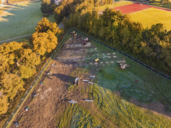 Construction site next to a sports field, surrounded by trees and shade, illuminated by morning light, PV FreifÃ¤chenanlage construction, Weil der Stadt, Germany