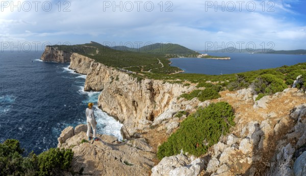 Tourist enjoying the view of steep cliffs by the sea, coastal landscape, cliffs on the Capo Caccia headland, Alghero, Sardinia, Italy