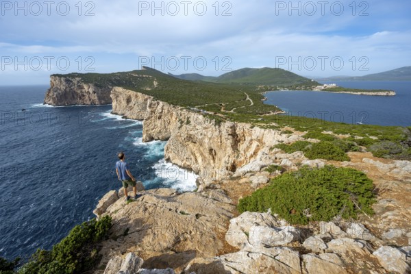 Tourist enjoying the view of steep cliffs by the sea, coastal landscape, cliffs on the Capo Caccia headland, Alghero, Sardinia, Italy