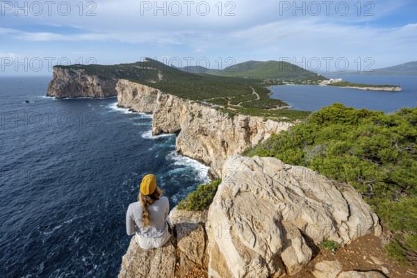 Tourist sitting on the edge of a steep cliff, view of steep cliffs by the sea, coastal landscape, cliffs on the Capo Caccia headland, Alghero, Sardinia, Italy
