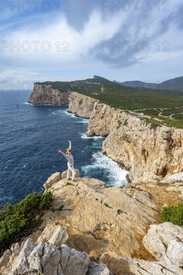 Tourist stretches her arms in the air, view of steep cliffs by the sea, coastal landscape, cliffs on the Capo Caccia headland, Alghero, Sardinia, Italy