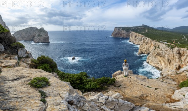 Tourist enjoying the view of steep cliffs by the sea and the rocky island of Isola Foradada, cliffs on the Capo Caccia headland, Alghero, Sardinia, Italy