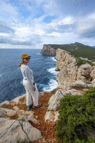 Tourist enjoying the view of steep cliffs by the sea and the rocky island of Isola Foradada, cliffs on the Capo Caccia headland, Alghero, Sardinia, Italy