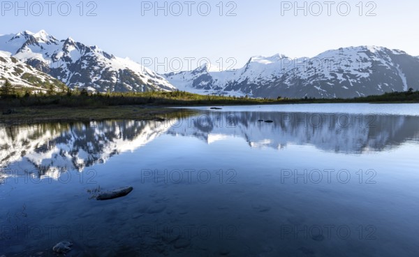 Mountain peaks with Portage Glacier glacier and snow reflected in Divide Lake mountain lake in evening light, Portage Pass Trail, Whittier, Alaska, USA