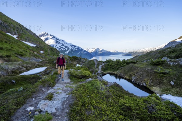 Hikers on Portage Pass, snow-covered mountains and Fjord Passage Canal, near Whittier, Alaska, USA