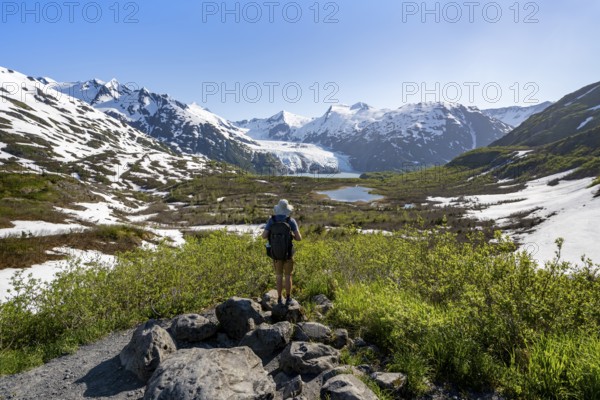 Hiker enjoys views from Portage Pass of Divide Lake, snowy mountain peaks and glaciers Portage Glacier, Portage Pass Trail, near Whittier, Alaska, USA
