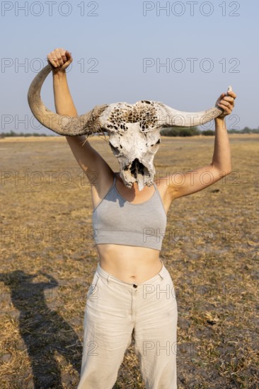 Young woman holding buffalo skull in front of her head, Lustig, Botswana