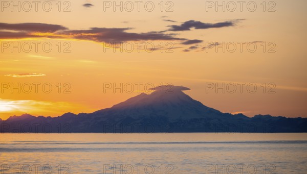 View of Cook Inlet on white mountain peaks of Mount Redoubt at sunset, picturesque golden light of the midnight sun, mountains of the Aleutian Range, Anchor Point, Anchor River State Recreation Area, Alaska, USA