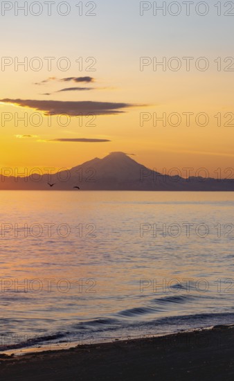 View of Cook Inlet on white mountain peaks of Mount Redoubt at sunset, picturesque golden light of the midnight sun, mountains of the Aleutian Range, Anchor Point, Anchor River State Recreation Area, Alaska, USA