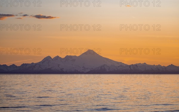View of Cook Inlet on white mountain peaks of Mount Iliamna at sunset, picturesque golden light of the midnight sun, mountains of the Aleutian Range, Anchor Point, Anchor River State Recreation Area, Alaska, USA