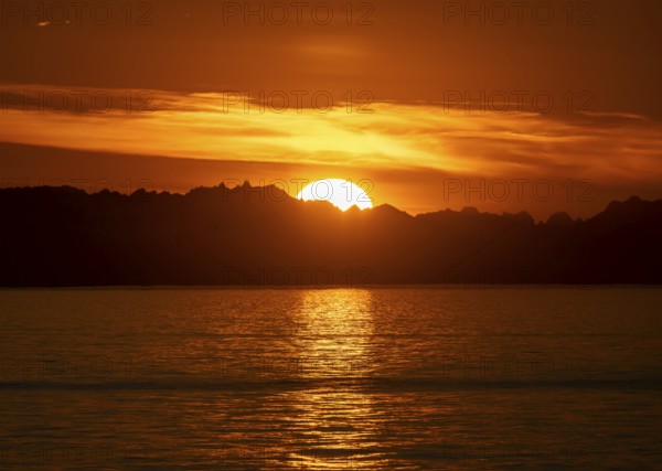 Sun sets behind mountain peaks, view of Cook Inlet at sunset, picturesque golden light of the midnight sun, mountains of the Aleutian Range, Anchor Point, Anchor River State Recreation Area, Alaska, USA
