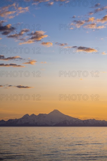 View of Cook Inlet on white mountain peaks of Mount Iliamna at sunset, picturesque golden light of the midnight sun, mountains of the Aleutian Range, Anchor Point, Anchor River State Recreation Area, Alaska, USA