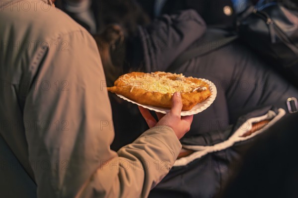 A person holds a plate of hot flatbread at a Christmas market, Christmas market 2025, Nagold, Black Forest, Calw district, Germany