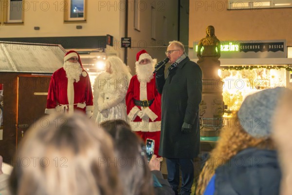 Two Santa Clauses stand with a woman and a speaker in front of an audience at a Christmas market, Christmas market 2025, Nagold, Black Forest, Calw district, Germany
