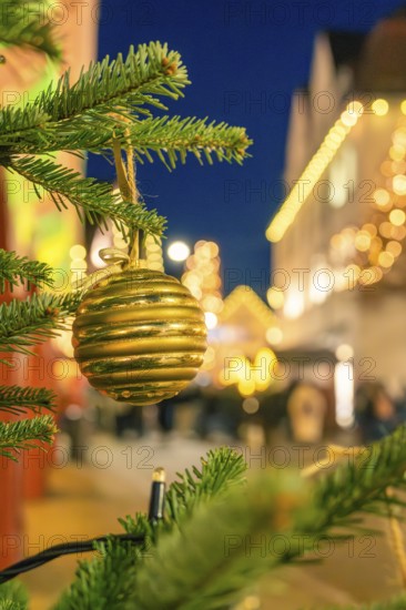 Golden Christmas ball on a pine branch surrounded by blurred lights, Christmas market 2025, Nagold, Black Forest, Calw district, Germany