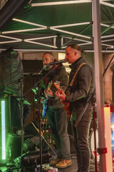 Two musicians on a stage at night playing guitars surrounded by festive lighting, Christmas market 2025, Nagold, Black Forest, Calw district, Germany