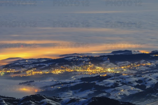 Night shot, long exposure of the 2506 meter high SÃ¤ntis into the wintery, snow-covered, fog-covered foothills of the Alps illuminated by the villages, during a clear full moon night, Canton of Appenzell, Switzerland