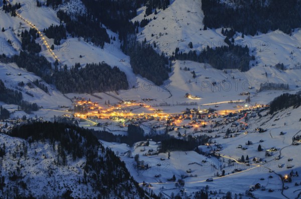Night shot, long exposure from 2506 meter high SÃ¤ntis into the wintry, snow-covered alpine landscape with the illuminated village of Wildhaus, during a clear full moon night, Canton of Appenzell, Switzerland