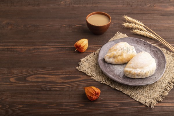 Glazed Pies with Cowberry jam on brown wooden background and linen textile, cup of coffee, side view, copy space