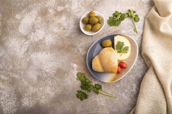 Smoked Mozzarella cheese, with tomatoes and olives on brown concrete background and linen textile, top view, flat lay, copy space