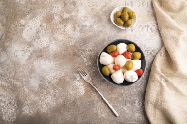 White Mozzarella cheese, with tomatoes and olives in blue bowl on brown concrete background and linen textile, top view, flat lay, copy space