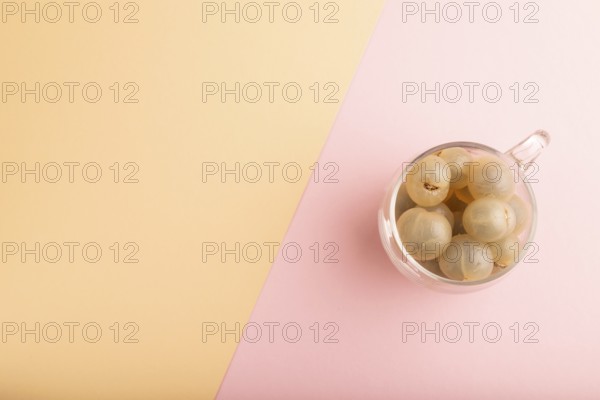 Ripe peeled Longan in glass on pink and orange pastel paper background, top view, flat lay, copy space, minimalism