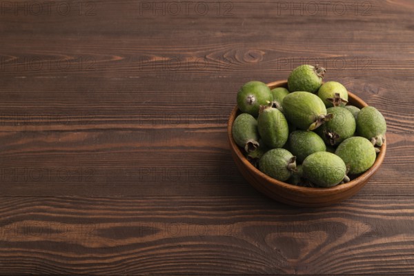 Ripe Feijoa in wooden bowl on brown wooden background, side view, copy space, minimalism