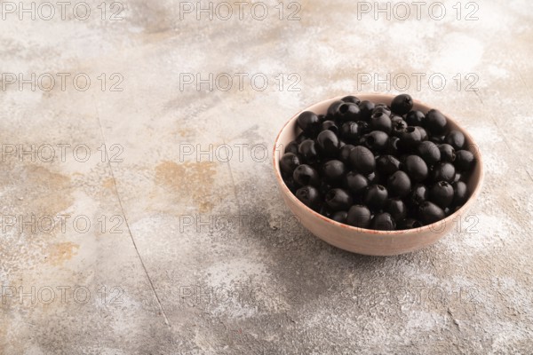 Fresh black olives in ceramic bowl on brown concrete background. side view, copy space