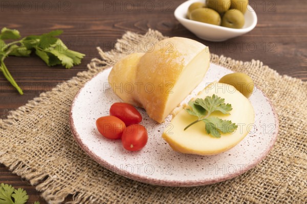 Smoked Mozzarella cheese, with tomatoes and olives on brown wooden background and linen textile, side view, close up