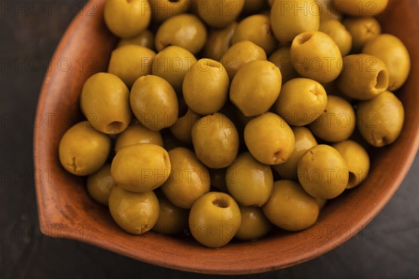 Fresh green olives in ceramic clay bowl on black concrete background. top view, close up, selective focus