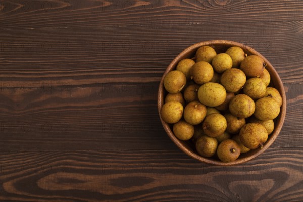 Ripe Longan in wooden bowl on brown wooden background, Top view, flat lay, copy space, minimalism