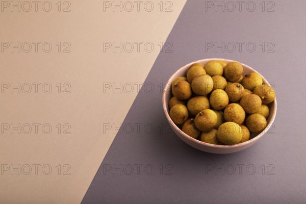 Ripe Longan in ceramic bowl on brown and gray pastel paper background, side view, copy space, minimalism