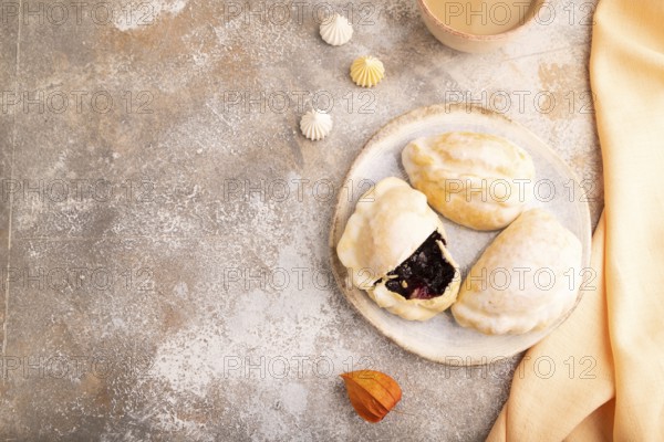Glazed Pies with blueberry jam on brown concrete background and orange linen textile, cup of coffee, top view, flat lay, copy space