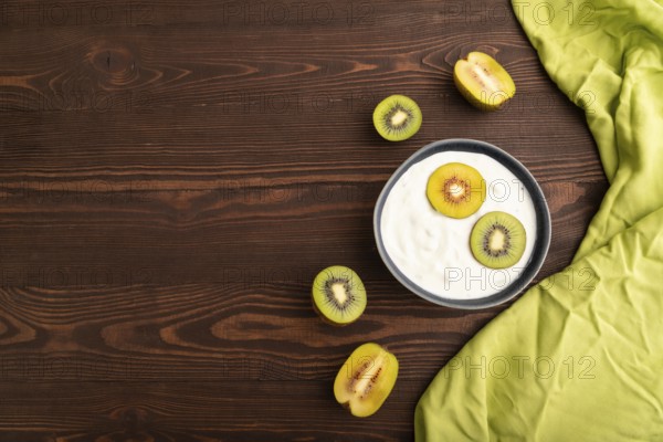 Yogurt, with kiwi in blue bowl on brown wooden background and green linen textile, top view, flat lay, copy space, minimalism