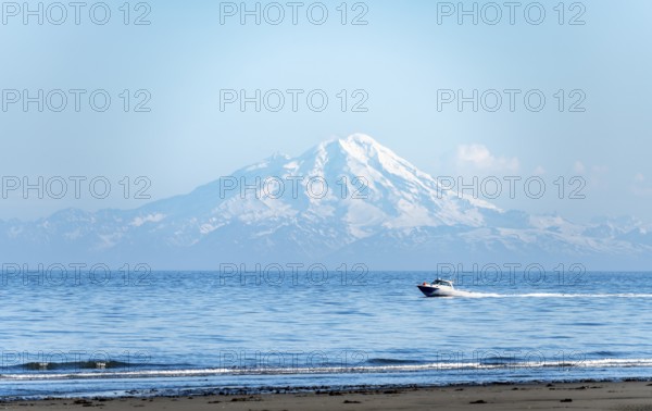 View over Cook Inlet to white mountain peaks of Mount Redoubt, motor boat rides on the ocean, Aleutian Mountains, Anchor Point, Anchor River State Recreation Area, Alaska, USA