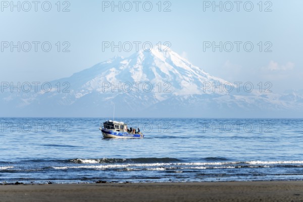 View of Cook Inlet on white mountain peaks of Mount Redoubt, mountains of the Aleutian range, motor boat on the ocean, Anchor Point, Anchor River State Recreation Area, Alaska, USA