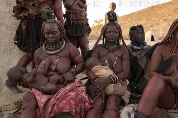 Married Himba woman with their babies in their arms sitting in front of the first woman's hut, in the morning, traditional Himba village, Kaokoveld, Kunene, Namibia