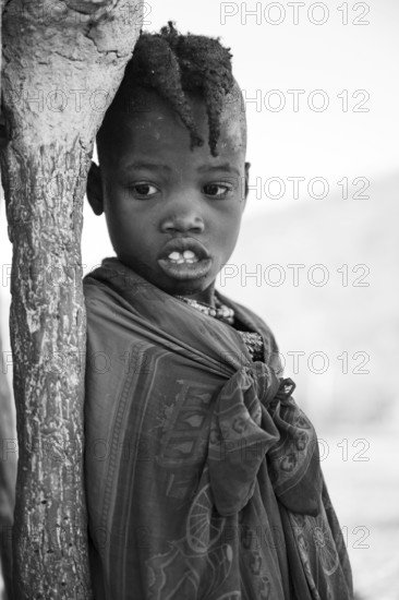 Black and white, Himba girl leaning at a traditional clay hut, in the morning, traditional Himba village, Kaokoveld, Kunene, Namibia
